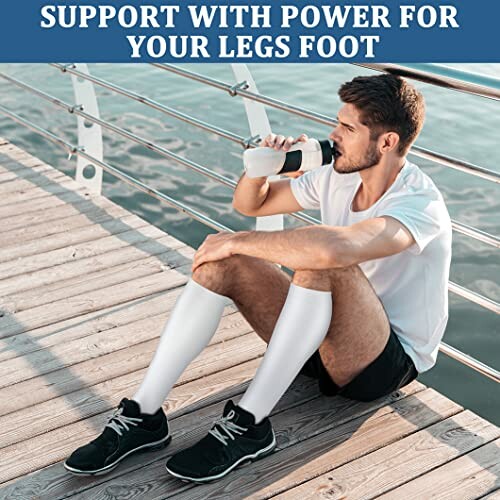 Man sitting on dock wearing compression socks and drinking water.